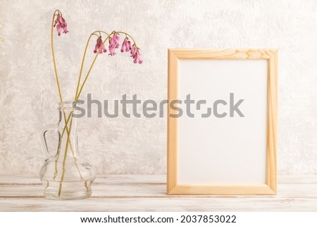 Wooden frame with pink dicentra, broken heart in glass on gray concrete background. side view, copy space, mockup, template, spring, summer minimalism concept.