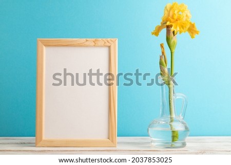 Wooden frame with yellow iris flower in glass on blue pastel background. side view, copy space, mockup, template, spring, summer minimalism concept.