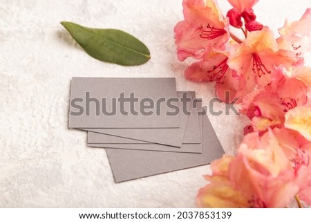 Gray business card with pink azalea flowers on gray concrete background. side view, copy space, mockup, template, spring, summer minimalism concept.
