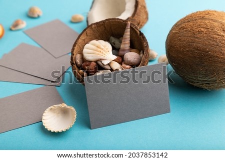 Gray paper business card with coconut and seashells on blue pastel background. Side view, copy space. Tropical, healthy food, vacation, holidays concept.