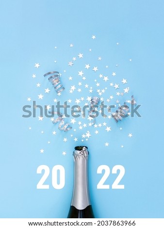 Open bottle of champagne on blue background decorated with silver star confetti and numbers 2022 . New Years celebration or party. Selective focus. Royalty-Free Stock Photo #2037863966