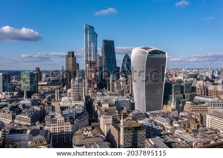 Aerial view of financial tower surrounded by small buildings in the beautiful city of London on a cloudy day with blue sky