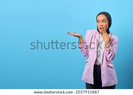 Surprised Asian woman showing product over blue background
