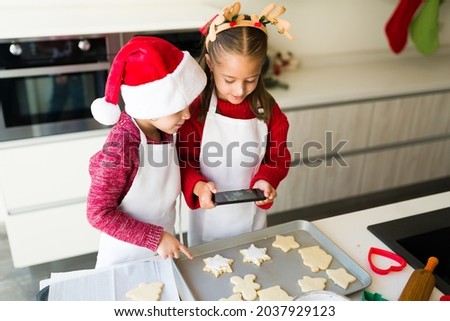 Beautiful kids wearing aprons taking a picture with a smartphone of the baked christmas cookies 