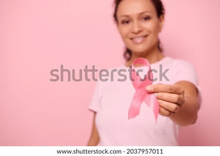 Blurred smiling mixed race woman in pink t-shirt hold satin ribbon in her hand. Breast and abdominal cancer awareness, October Pink day on colored background, copy space. Breast cancer support concept Royalty-Free Stock Photo #2037957011
