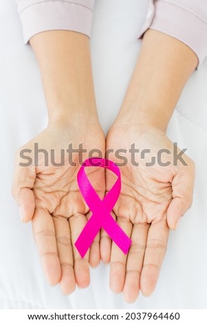 Pink ribbon, on aged hand of illness woman survivor, representing international fabric symbol of breast cancer awareness to give moral support and express willing to fight against chest tumor disease
