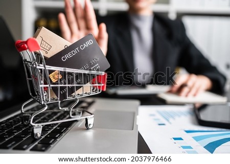 Close up of credit card and small parcel box in a mini shopping cart on laptop keyboard with businesswomen refusing in the background, e-commerce, business online concept.