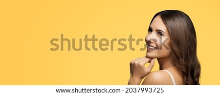 Portrait of looking up, cheerful smiling, thinking woman, isolated over yellow color background. Brunette girl posing at studio. Wide composition with copy space free area for some text. Female model.