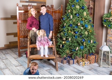sister and brother and their parents stand in a living room near new year tree
