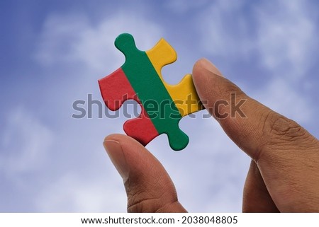 Hand holding piece of jigsaw puzzle with flag of Lithuania. Jigsaw puzzle of Lithuania flag on sky background.