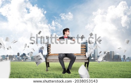 young businessman sits on a bench with an empty banner. around in the chaos flying documents