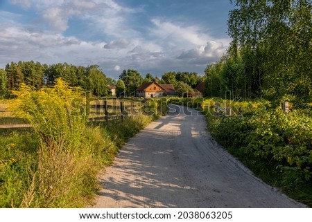 End of summer in the village of Warmia - a dirt road in the village of Redykajny near Olsztyn, by the road yellow flowers, wooden fences and trees Royalty-Free Stock Photo #2038063205