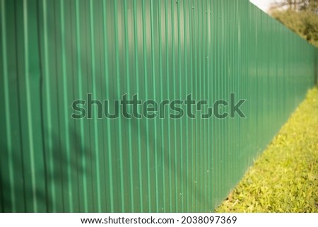 Green fence. Metal fence made of profile sheet. The territory is fenced with a high fence. Ribbed surface on the street. Shooting diagonally.
