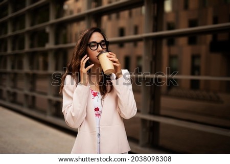 Young businesswoman talking to the phone. Female manager drinking coffee while walking through the city