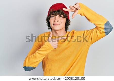 Handsome young man wearing wool hat smiling making frame with hands and fingers with happy face. creativity and photography concept. 