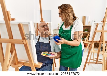 Middle age hispanic painter couple smiling happy painting and using smartphone at art studio.