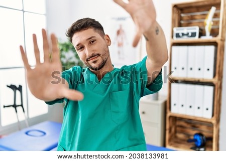 Young physiotherapist man working at pain recovery clinic doing frame using hands palms and fingers, camera perspective 