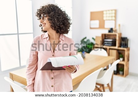 Young middle eastern woman wearing business style at office looking to side, relax profile pose with natural face and confident smile. 