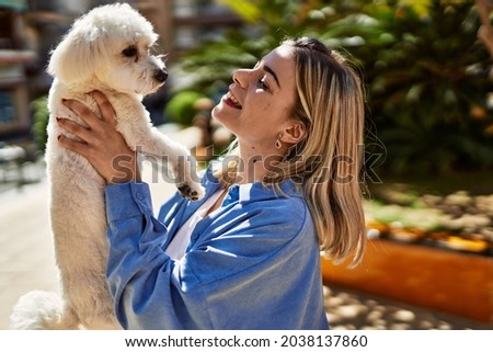Young blonde girl smiling happy holding dog at the city.