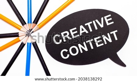 On a light background, multi-colored pencils and on a black background a white card with the text CREATIVE CONTENT