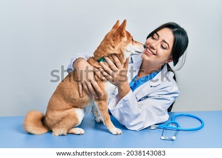 Veterinarian woman wearing uniform at the clinic, hugging dog with love Royalty-Free Stock Photo #2038143083