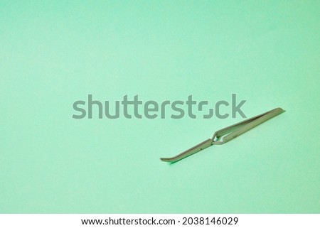 metal tweezers on a green background.