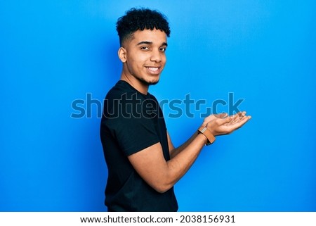 Young african american man wearing staff t shirt pointing aside with hands open palms showing copy space, presenting advertisement smiling excited happy 