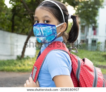 Close up of an Indian girl child student in blue school uniform with red bag and nose mask protection going to school