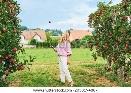Outdoor portrait of happy young woman in countryside, female model throwing apple in the air