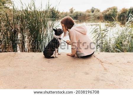 Little girl kissing her Boston Terrier dog on the lakeshore - Autumn scenery - copy space