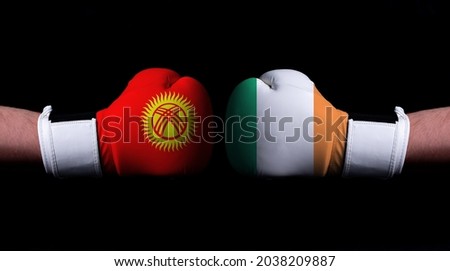 Two hands of wearing boxing gloves with Ireland and Kyrgyzstan flag. Boxing competition concept. Confrontation between two countries
