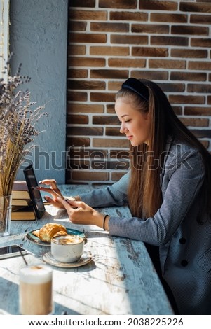 A young woman makes purchases through mobile applications. Makes an online payment on a tablet. Women's purchases through online stores.A girl is sitting in a cafe at breakfast.