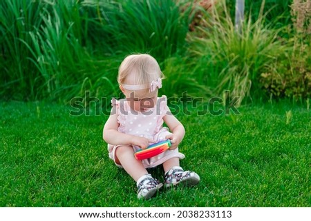 Girl playing with pop it sits on green grass in a dress