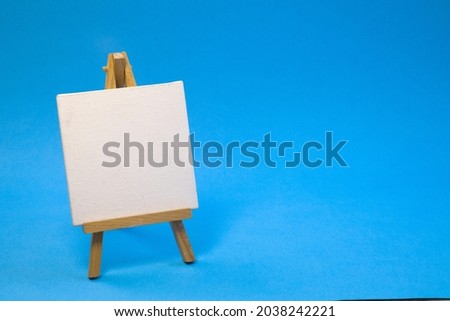 Small empty wooden easel on bright blue background, close up with copy space