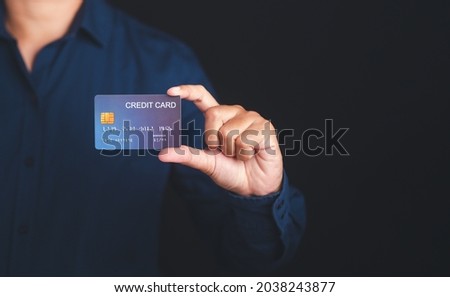 Hand of holding a mockup blue credit card while standing with a black background in the studio. Close-up photo. Money and business concept.
