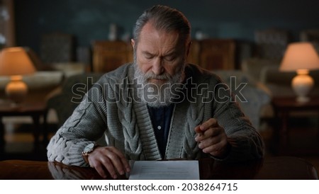 Focused senior business man signing agreement in home office. Serious old businessman reading contract in vintage house. Senior man checking documents in classic cabinet. 