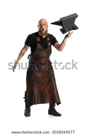 Flying huge anvil. One bearded bald man, blacksmith wearing leather apron or uniform having fun isolated on white background. Concept of labor, retro professions, power, beauty, humor. Funny meme