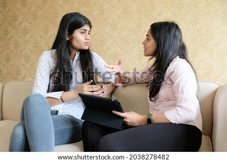 Two young Indian girls having discussion while using a digital tablet at home Royalty-Free Stock Photo #2038278482