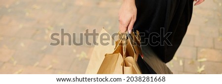 Banner of Incognito woman holding several paper bags with purchased things walking outdoors in the park, girl after shopping. Black Friday