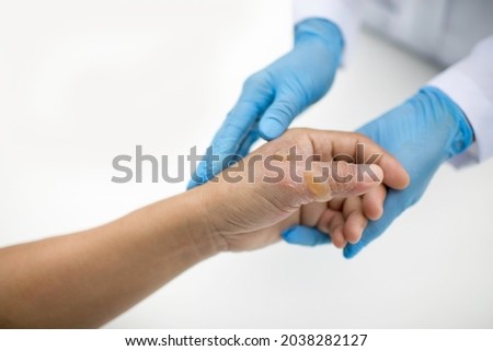 Doctor holding patient's hand and thumb with burn injuries. Nurse with gloves attending a man's blisters.Wound care in hospital.White background.Medical officer treating patient with serious burns. Royalty-Free Stock Photo #2038282127