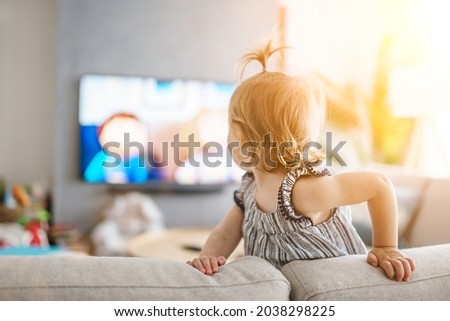 A cute little girl from back watching tv at home