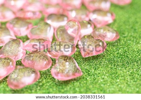 Pink transparent plastic hearts on green glittering background.