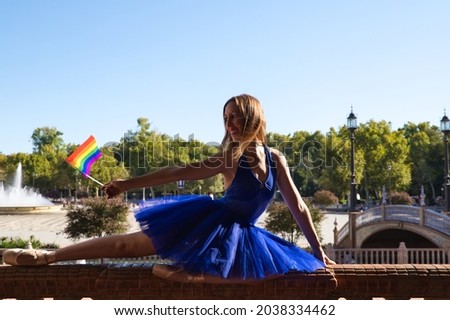 classical ballet dancer and lesbian leaning on a railing in a park. holding the gay pride flag in her hand. Concept of homosexuality and ballet