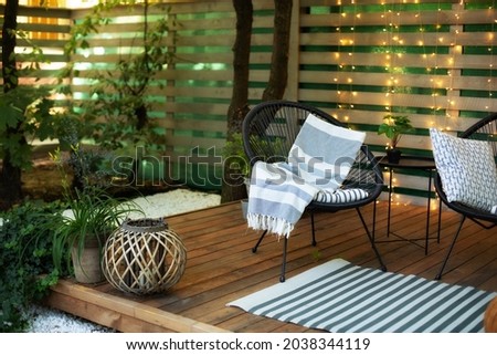 Exterior veranda of house with black Acapulco armchairs and plants pots. Cozy space in patio or balcony with garland. Interior Wooden verande with garden furniture. Modern lounge outdoors in backyard Royalty-Free Stock Photo #2038344119