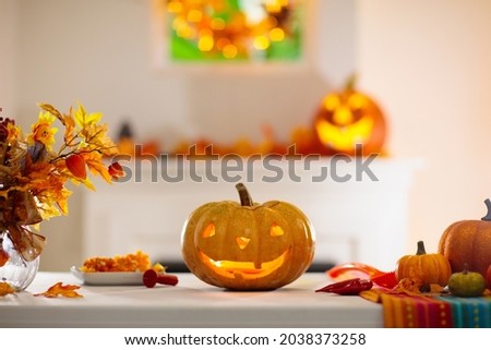 Woman carving pumpkin for Halloween celebration. Female in apron cutting jack o lantern for traditional trick or treat decoration. Decorated living room with golden autumn leaves wreath over fireplace