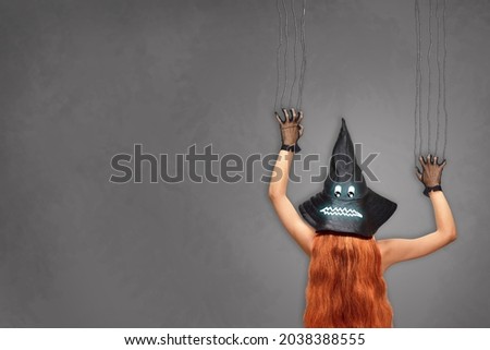 A witch in a witch's hat is scratching a gray wall with her claws. Halloween costume with a terrifying hat. Template for a postcard for all saints' day