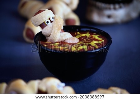 Fun food for kids. Mummy hot dogs on a blue rustic table sitting inside of a bowl of ketchup and mustard dip, with spider web design. Selective focus with blurred foregound and background.