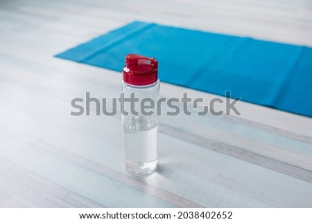 blue yoga mat and sports bottle stands on the floor, yoga preparation or training, sports at home during self-isolation and pandemic, training programs with a personal trainer online, taking care of