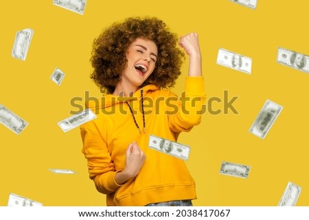 Money rain. Yes I did it! Portrait of joyous winner rich young woman in yellow hoody standing screaming and closed eyes, celebrating victory and richness. indoor isolated on yellow background