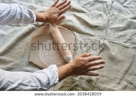 master craftsman rolls clay on the table, transfers napkin pattern to clay mass